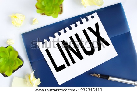 Linux. text on white notepad paper on blue folder. on a light background near the crumpled stickers and plants.
