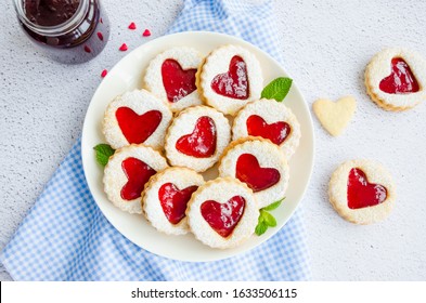 Linzer cookies with heart with raspberry jam and powdered sugar on a white plate with a cup of tea. Dessert on Valentine's Day. Horizontal orientation, top view.