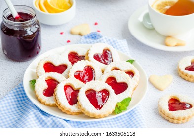 Linzer cookies with heart with raspberry jam and powdered sugar on a white plate with a cup of tea. Dessert on Valentine's Day. Horizontal orientation.