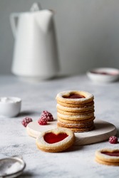 Linzer Cookies With Raspberry Jam Hearts Are Stacked On A Small Wooden Board On A Gray Table. Household Items.