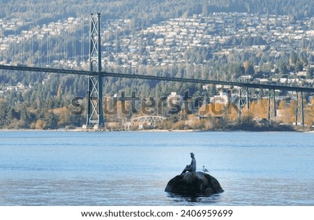 The Lions Gate Bridge next to the Girl in a Wetsuit bronze sculpture at Stanley Park during a fall season in Vancouver, British Columbia, Canada