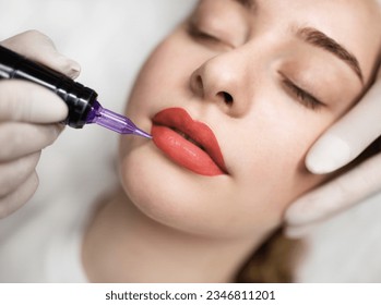 Lip Blushing. Cosmetologist applying permanent make up on lips of beautiful woman, closeup of attractive young female getting pmu treatment in beauty studio, artist using tattoo pen machine