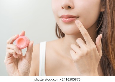 Lip care protection concept, asian young woman, girl applying balm from jar, taking with finger, touching on dry mouth from natural beauty product, skincare routine, makeup and cosmetics on background - Powered by Shutterstock