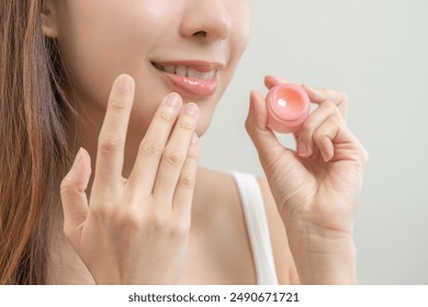 Lip care protection concept, asian young woman, girl applying balm from jar, taking with finger, touching on dry mouth from natural beauty product, skincare routine, makeup and cosmetics on background - Powered by Shutterstock