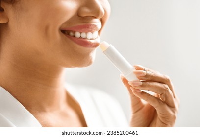 Lip Care. Unrecognizable young black woman applying moisturising chapstick on lips, closeup of smiling african american female using nourishing lip balm while making beauty routine at home, cropped