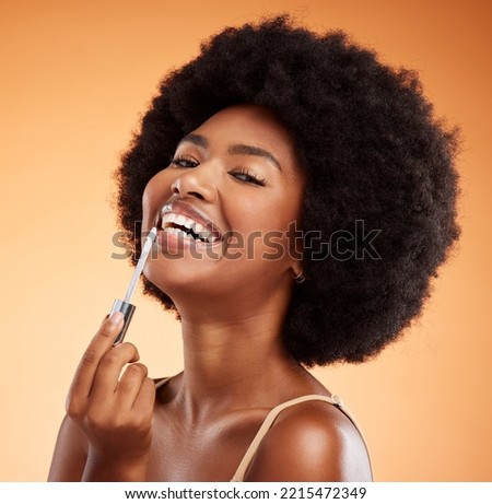 Lipgloss, smile and black woman excited about makeup against an orange studio background. Face portrait of a young African girl model with lipstick and cosmetic beauty product for care of lips