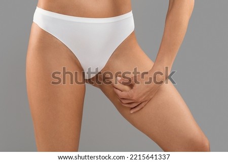 Liposuction Concept. Slim Woman In White Panties Touching Inner Thigh Skin, Unrecognizable Young Female In Underwear Enjoying Result Of Slimming, Standing Isolated On Grey Background, Cropped