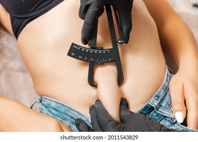 Liposuction. Doctor of aesthetic cosmetology measures the fat sediments on the client's stomach with a caliper. Close up. Top view. Professional cosmetology in a beauty salon.