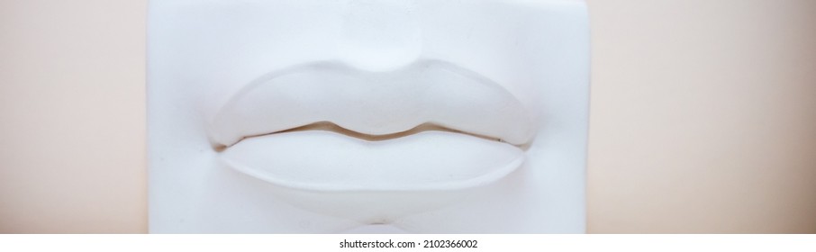 Lips Plaster Casting In A Sculpting Studio Used For Clay Modelling Workshops By Sculptors.White Plaster Lips On Pastel Background. Cosmetologist,permanent Makeup, Lip Augmentation