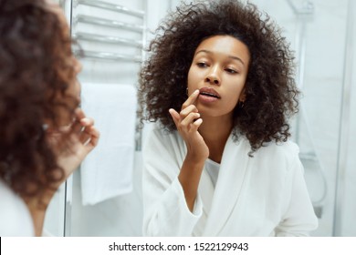 Lips Skin Care. Woman Applying Lip Balm Looking In Mirror At Bathroom. Portrait Of Beautiful African Girl Model With Beauty Face And Natural Makeup Applying Lip Product With Finger