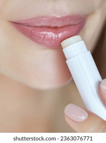 Lips skin protection. Close up portrait of beautiful woman holding a lipstick and applying hygienic balm. Natural make up