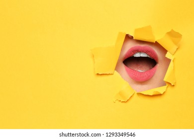 Lips of young woman with beautiful lipstick visible through hole in color paper. Space for text