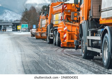 Liptovsky Hradok, Slovakia - February 12, 2020: Group of bright orange highway maintenance trucks with de icing salt getting ready on winter, snow covered road