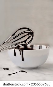 A liquid dark chocolate flows down the whisk into a white plate. chocolate streams - Shutterstock ID 2356559685