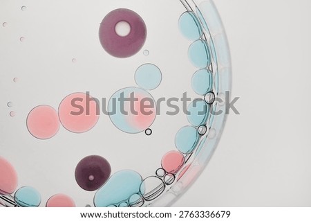 Liquid droplets in multiple colors floating and merging inside clear petri dish