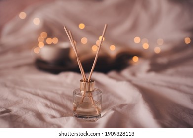 Liquid home perfume in glass bottle with sticks over glowing lights in bed at home close up. Cozy atmosphere concept. Freshness.  - Shutterstock ID 1909328113