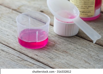 Liquid Medicine In Plastic Glass On Wooden Table.