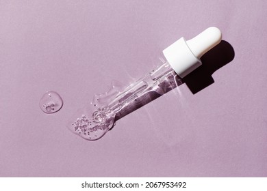 Liquid Oil Serum Drop In Pipette Isolated On Pastel Violet Background. Retinol, Aha Acid, Collagen Skincare Fluid, Photo With Shallow Depth Of Field. Hyaluron Essence In Dropper For Beauty Treatment.