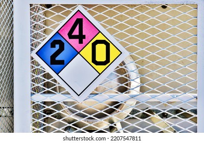 Liquid Petroleum Gas Cylinder Stored Horizontally In A Metal Safety Cage With A Hazardous Materials Classification Placard, Eye Level Front View.