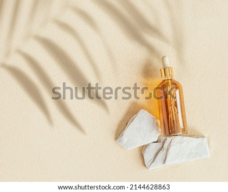 Liquid product package in glass bottle on stone stand, fine sand background with palm leaf shadows. Cosmetics mock up. Japanese zen garden with rounds on sand. Facial cosmetics, top view