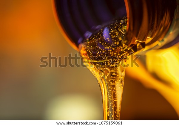 Liquid stream of motorcycle motor oil flows\
from the neck of the bottle\
close-up.