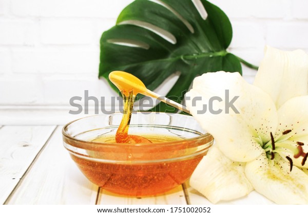 Liquid sugar paste for hair removal in a\
glass bowl with lily flower and dracaena leaf. The concept of body\
care, beauty treatments.