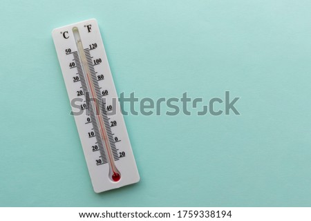 Liquid thermometer. Light green background. White plastic case, red alcohol. Two scales in degrees - celsius, fahrenheit. Temperature value is 33 C or 92 F.