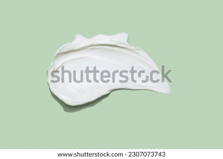 Liquid white cream smear isolated on green background. Beauty cosmetic smudge such as hair conditioner, creamy lotion, facial retinol serum, mask balm, cleanser, shower gel or shampoo top view