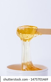Liquid yellow sugar paste or wax for depilation on a wooden stick close-up on a white background - Shutterstock ID 1475701469