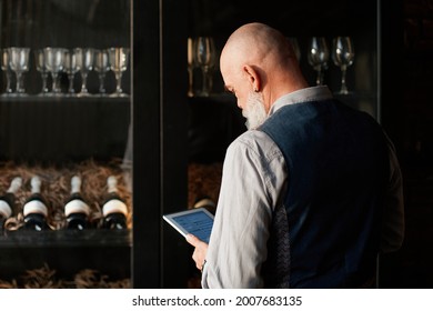 Liquor Store Owner With A Digital Tablet Standing Near A Rack Of Wine Samples .