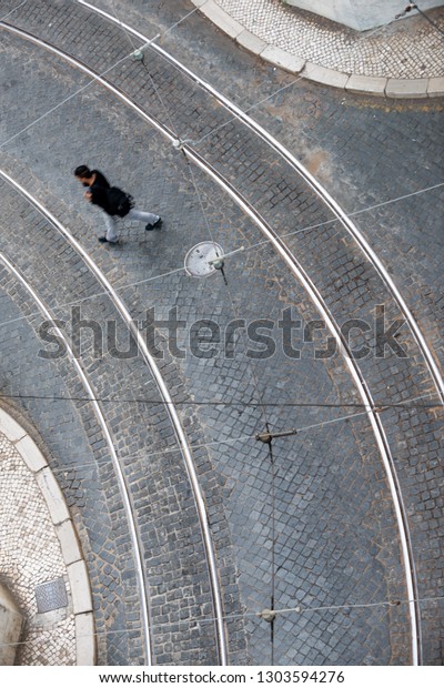 Lisbon cobblestone curved street aerial\
with tram tracks and pedestrian crossing\
street.