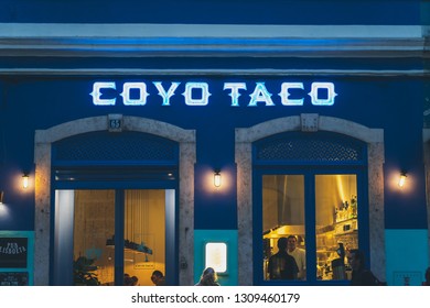 Lisbon, Portugal - 01/03/19: Coyo Taco Shop Front Blue Color, Exterior Shot Warm Yellow Lights People Inside Restaurant Near Principe Real.