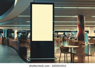 Lisbon, Portugal - August 5, 2021: A Blank Vertical Advertising Billboard In Front Of A Crowded Mall Food Court With Tables And Customers In A Background. An Empty LCD Screen Template In A Restaurant