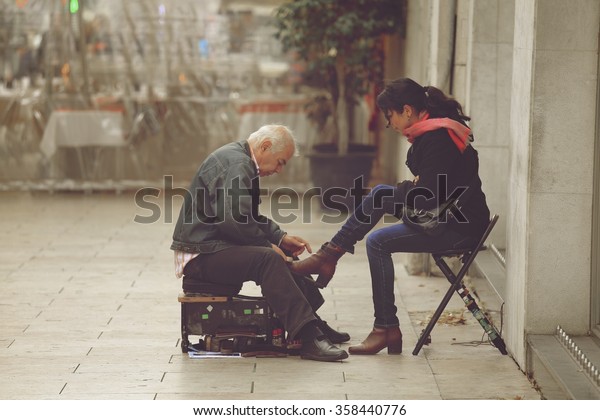 LISBON, PORTUGAL -\
DECEMBER 22 2015: Shoeshine man working on client\'s shoe on a\
street in Lisbon, Portugal. Lisbon is very traditional in its\
ancient streets find\
shoeshine\
