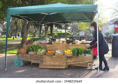 Lisbon - Portugal - February 27, 2021: Farmer Market On Principe Real Park In The Historic Center.  A Young Female Seller Is Working On Her Stand Of Vegetables And Fruits. 