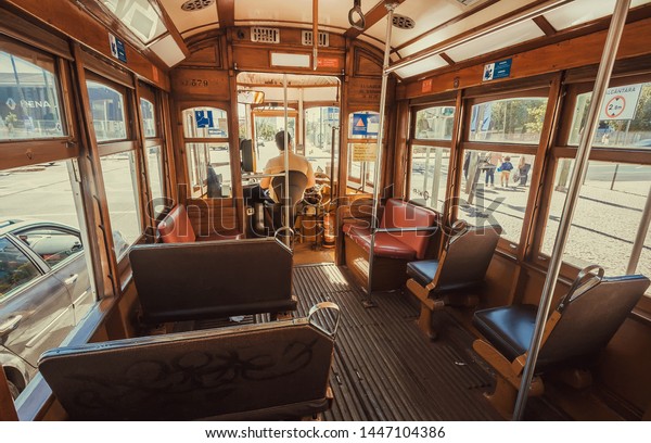 LISBON, PORTUGAL: No passengers inside retro tram\
and a driver in cabin moving vehicle past modern districts of city\
on 19 May, 2019. Portuguese language has 250 million total speakers\
around world