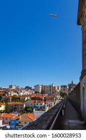 LISBON, PORTUGAL - OCTOBER 10, 2019: Plane Flying Over Águas Livres Aqueduct With Cityscape On A Background.