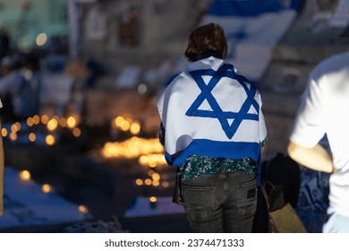 Lisbon, Portugal October 10, 2023. A woman at the memorial to the fallen Israelis in October 2023 at dusk, , with the flag of Israel on her shoulders - Powered by Shutterstock