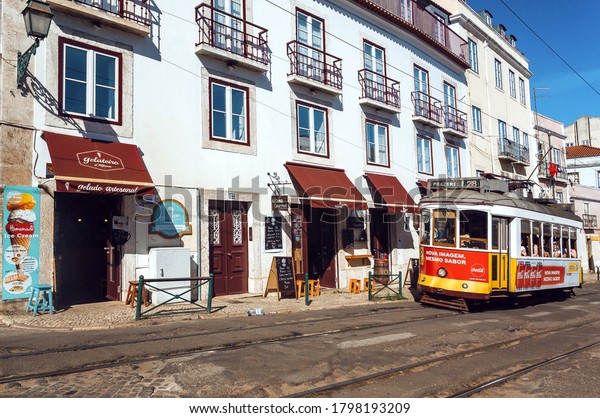 LISBON,\
PORTUGAL: Old city street with moving tramway on tram rails, past\
rustic houses in sunny capital on 18 May, 2019. Portuguese language\
has 250 million total speakers around the\
world