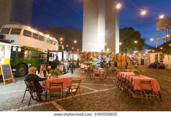LISBON, PORTUGAL: People having late dinner at\
outdoor restaurant on urban area with tables and some fast food\
trucks for customers on 17 May, 2019. Portuguese language has 250\
million total speakers