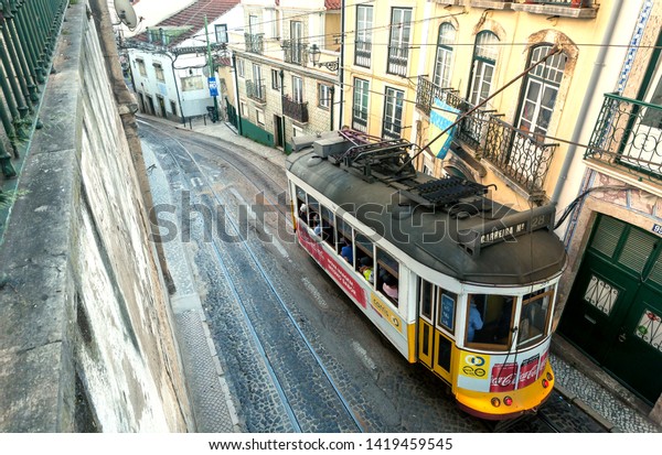 LISBON, PORTUGAL: Retro tram car driving past\
houses on small narrow street, like a tourist attraction on 17 May,\
2019. Portuguese language has 250 million total speakers around the\
world