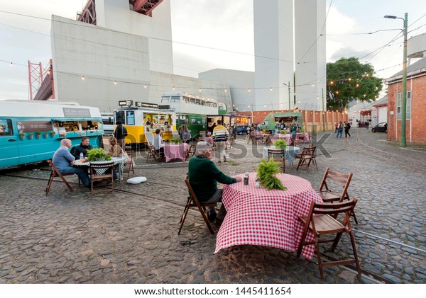 LISBON, PORTUGAL: Urban cityscape with people\
relaxing at outdoor restaurant with fast food trucks on street on\
17 May, 2019. Portuguese language has 250 million total\
speakers