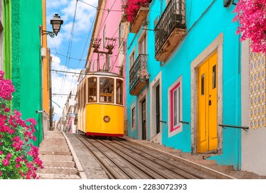 Lisbon, Portugal - Yellow tram on a street with colorful houses and flowers on the balconies - Bica Elevator going down the hill of Chiado