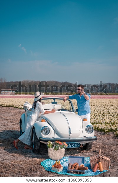 Lisse Netherlands April 2019, A classic, white
Volkswagen Beetle car on a flower covered meadow in the bulb
region. Men and w posing by old classic car by the flower fields in
the bulb region Holland 