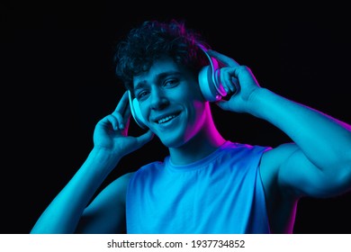 Listen to music  Half  length portrait young man in headphones isolated multicolored dark background in neon light  Concept human emotions  youth culture  Copy space for ad 