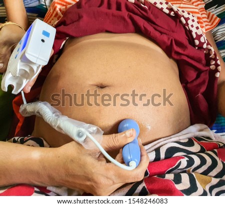 listening to fetal heart sound on a pregnant woman belly by a fetal doppler machine by a trained female health worker at indian home