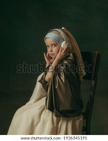 Listening to music with headphones. Medieval little girl as lady with a pearl earring on dark studio background. Concept of comparison of eras, childhood, ancient. Stylish, creative, art vision.