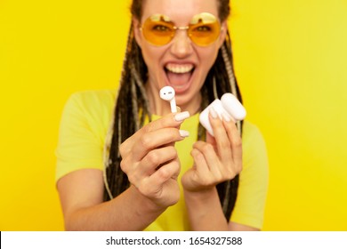Listening music on airpods. Cheerful woman in the yellow studio with white airpods.