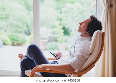 listening relaxing music at home, relaxed man in headphones sitting in deck chair in modern bright interior - Powered by Shutterstock