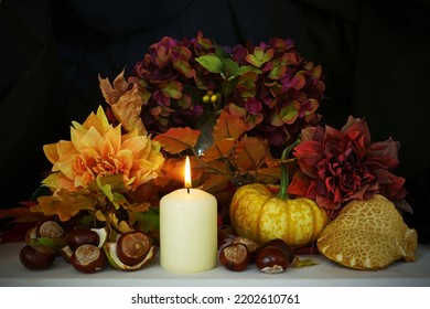 A lit candle with autumn flowers, pumpkin, fungus, horse chestnuts and Hydrangeas displayed as a table decoration with dark background. - Powered by Shutterstock